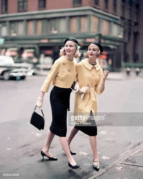 Two models crossing city street: (left) one wearing classic navy sheath with short yellow jacket by Jeanne Campbell for Sportwhirl, beret by John Frederics Charmer, pins by Tiffany and Co., and I. Miller pumps; the other wearing knee-high coat worn over sleeveless chemise by Jeanne Campbell for Sportwhirl , T-strapped shoes by Fortunet, necklace by Colette, Kislav gloves, and Capador beret. (Photo by Sante Forlano/Condé Nast via Getty Images)